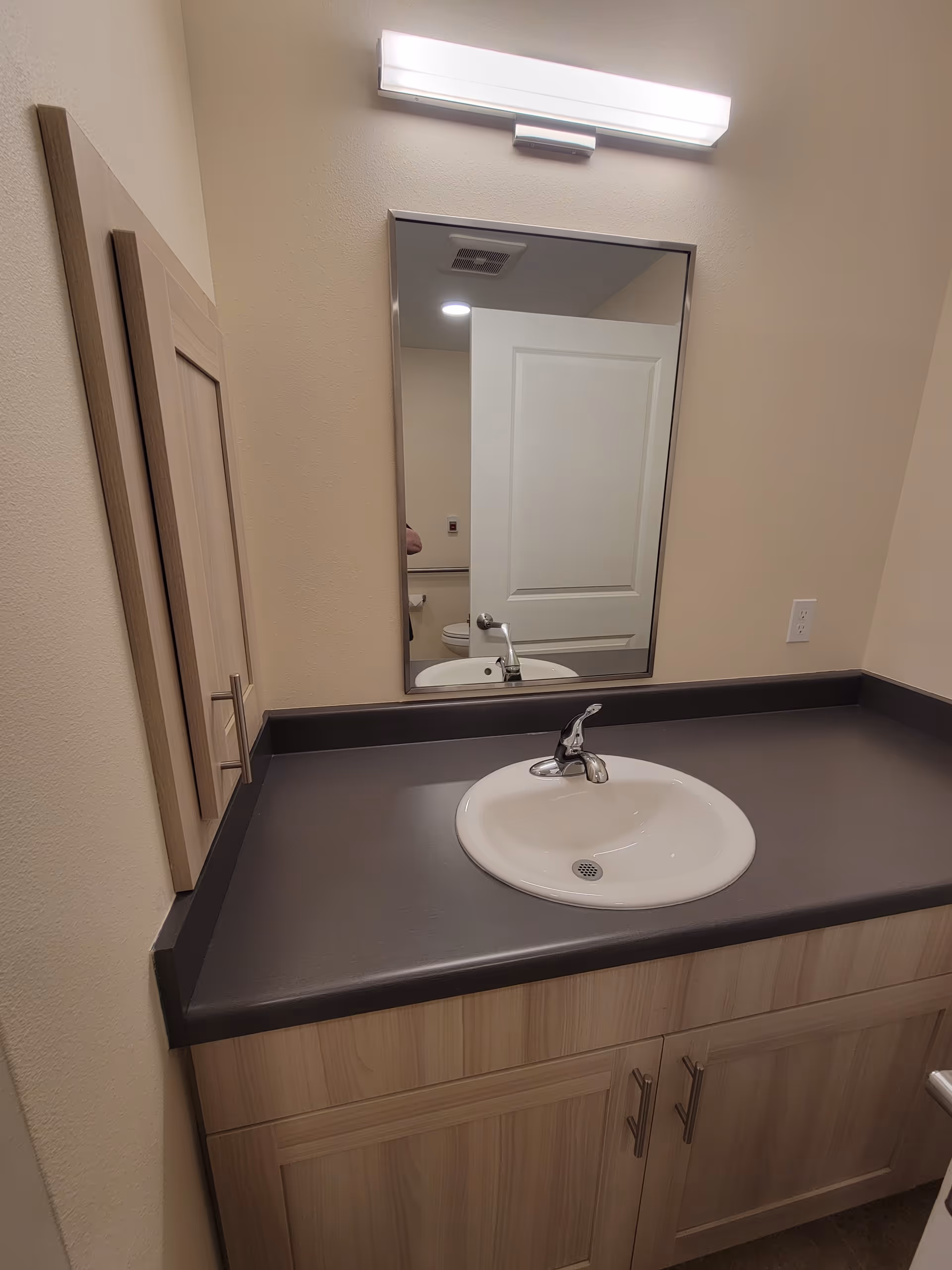 Bathroom vanity with sink, mirror, cabinet storage, and overhead fluorescent light.