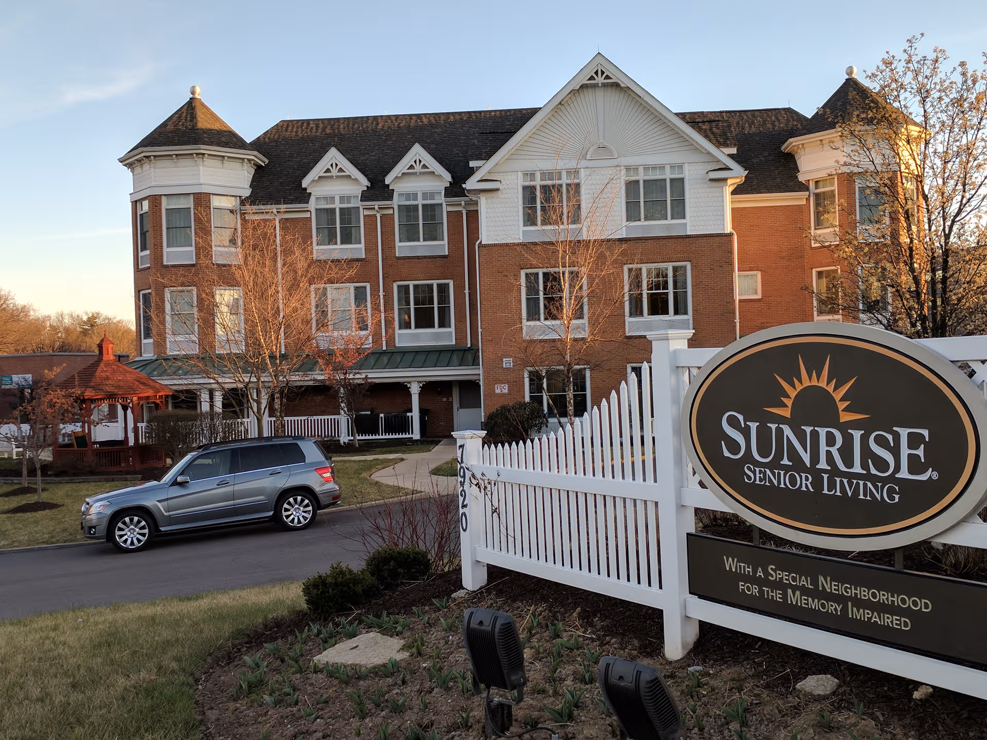 Front exterior of a brick senior living building with a white fence and Sunrise sign.