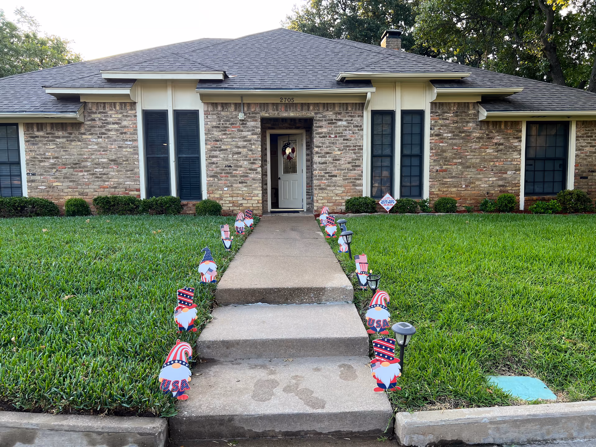 Brick assisted living building front with patriotic lawn decorations and a central entry walkway.