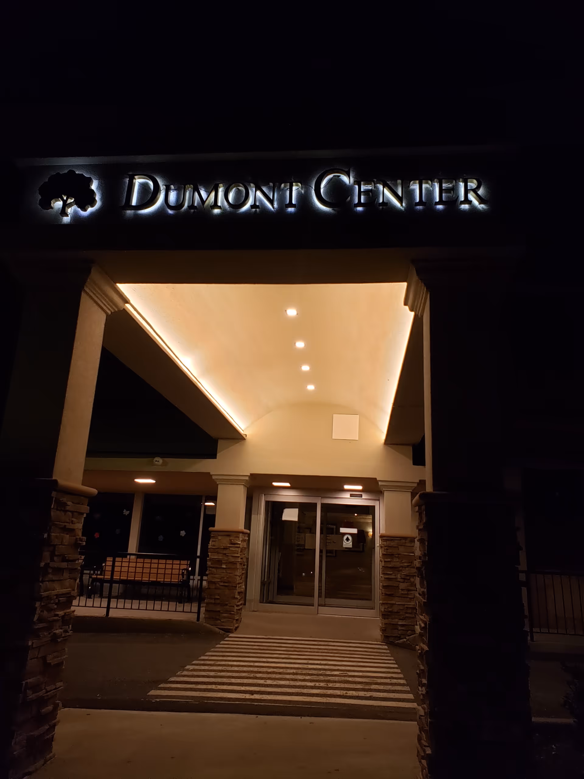 The illuminated Dumont Center sign above the glass entrance of a building at night.