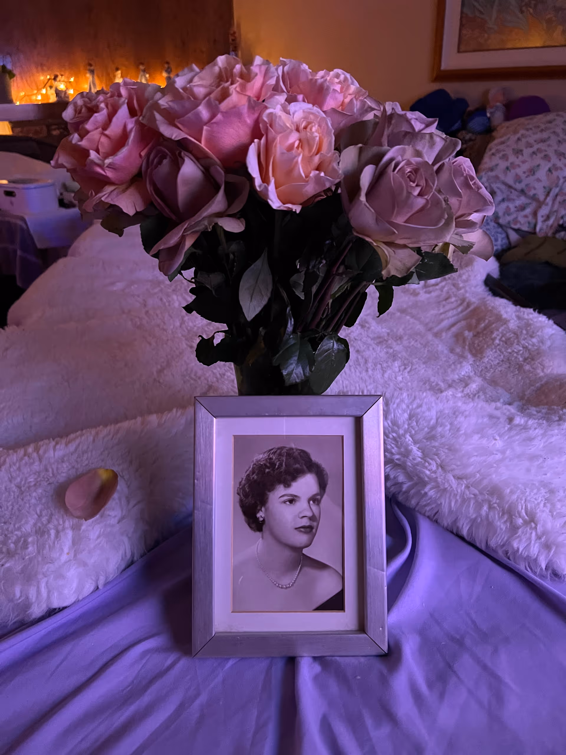 Bouquet of pink roses in a vase on a bed beside a framed photo.