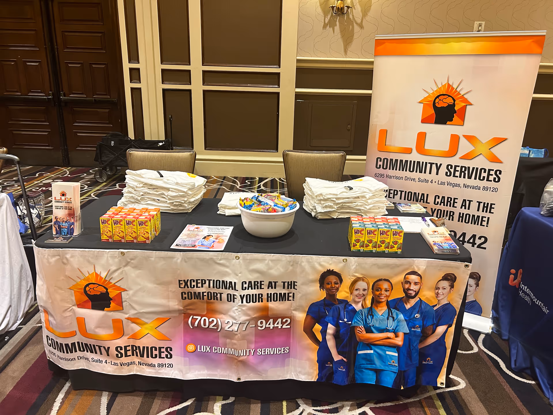 Indoor booth for LUX Community Services with banners, brochures, and candy bowls.