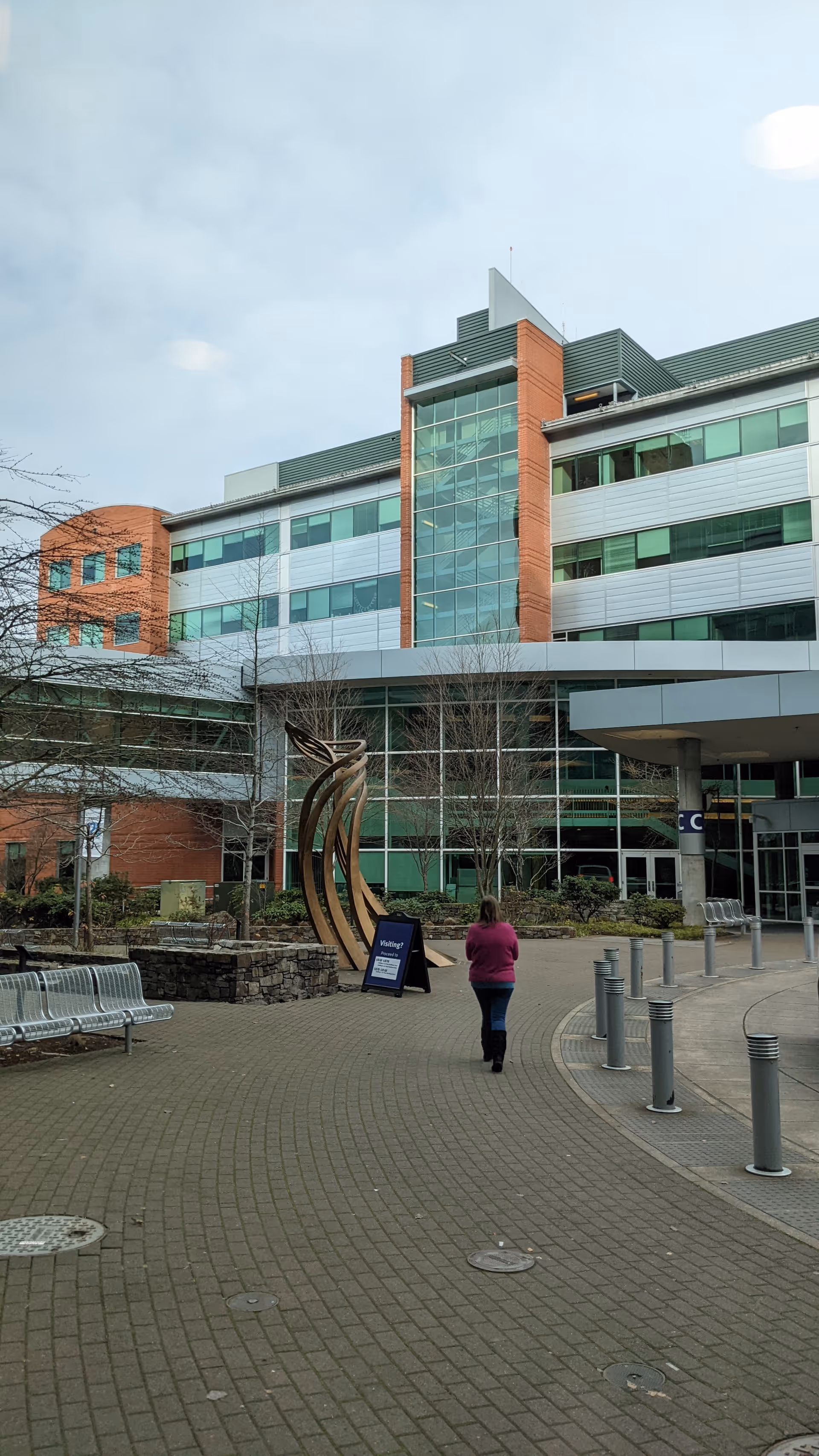 Exterior view of a modern medical facility with glass facade, walkway, and sculpture.