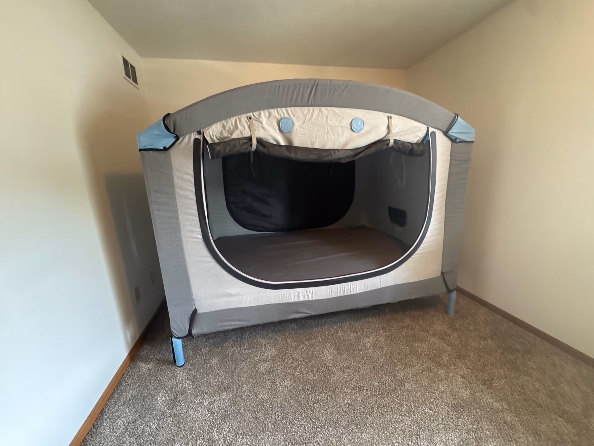 Indoor room featuring a gray pop-up tent set up on carpet.