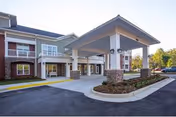 Exterior view of senior living facility entrance with a covered porte-cochère and landscaping.
