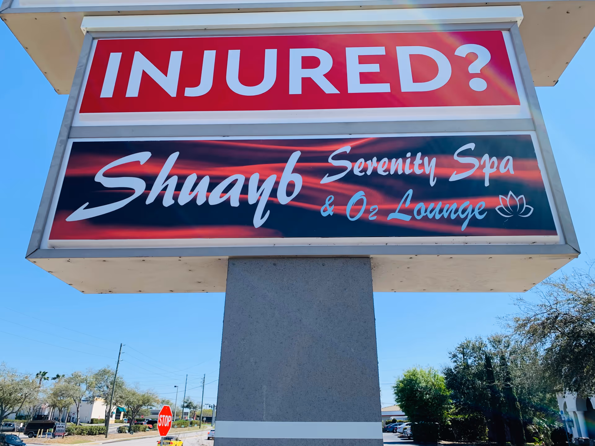 Outdoor sign on a concrete pedestal advertising 'INJURED?' and 'Serenity Spa & O2 Lounge'.