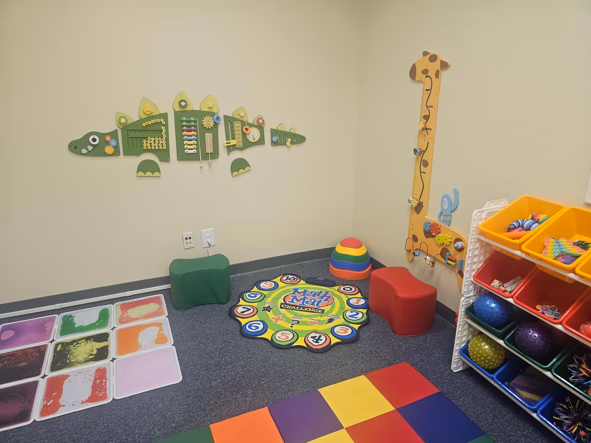 Colorful indoor playroom with a giraffe height chart, soft mats, and toy shelves.