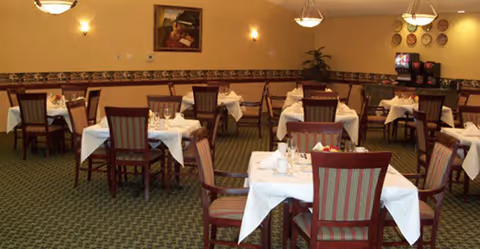 Empty dining room with white tablecloths and striped chairs in a senior living facility.