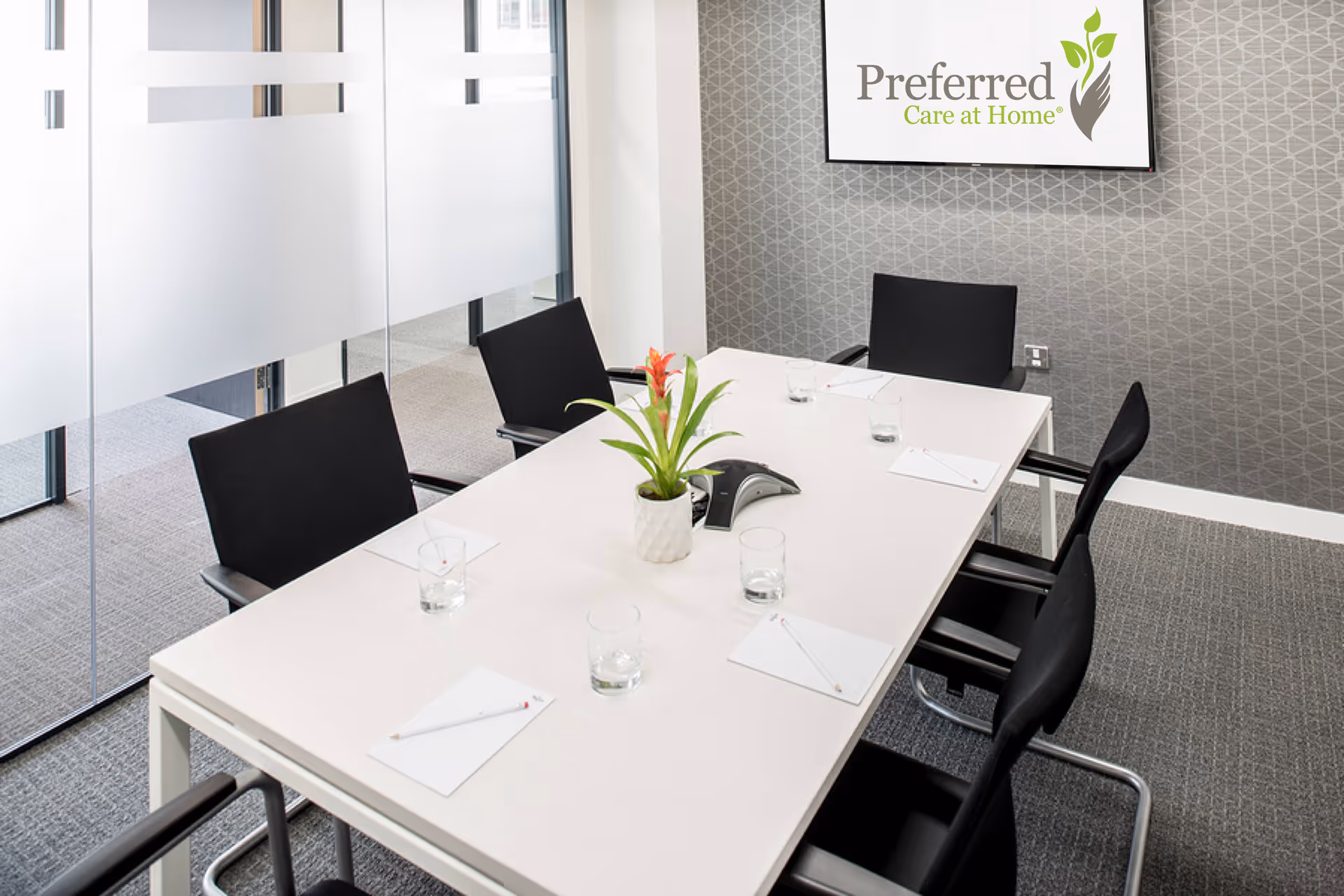 A modern conference room with a long white table, black chairs, and a wall logo.
