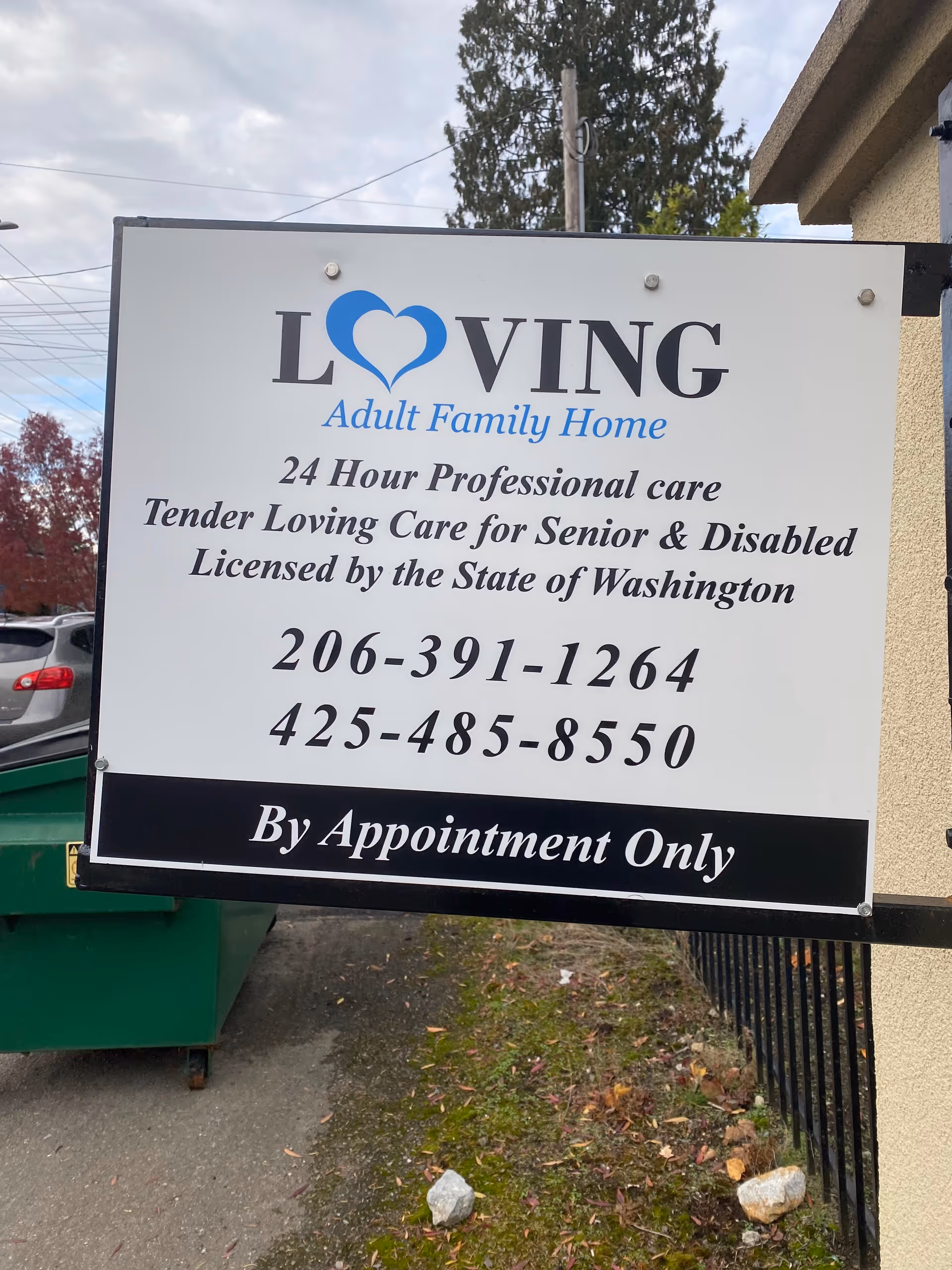 Large white sign for Loving Adult Family Home with contact numbers outside.