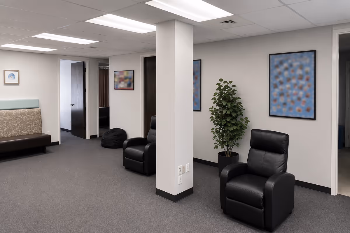 Neutral lounge area with black leather chairs, plant, bean bags, and abstract wall art.