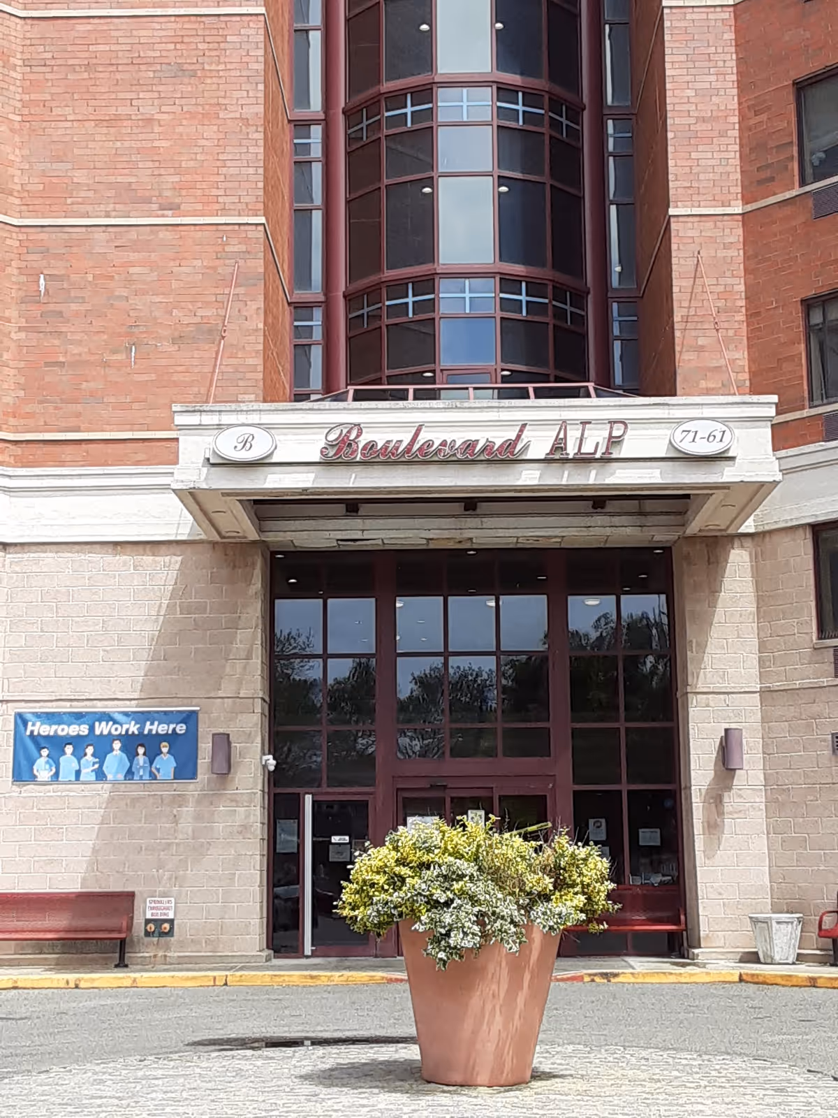 Brick building entrance with Boulevard Alp sign and glass doors, plus a large potted plant.