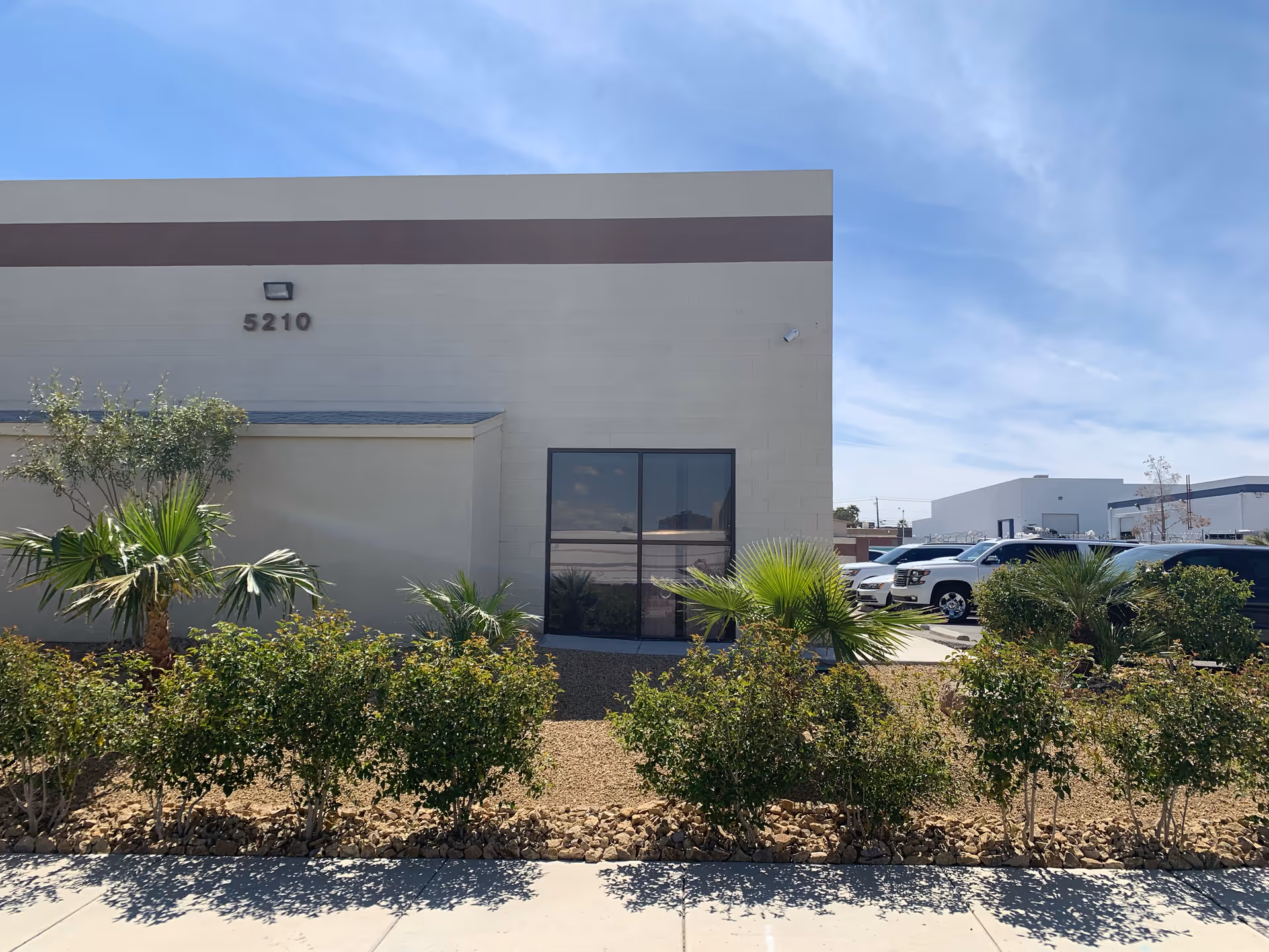 Front view of a beige building with a parking lot and desert landscaping.