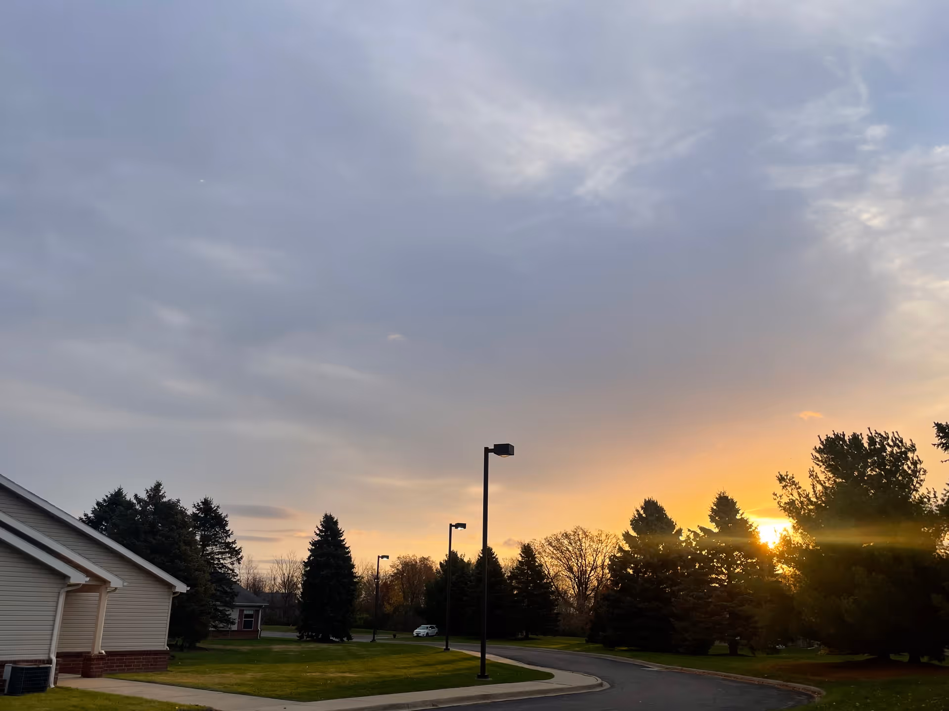 Sunset view over a suburban care facility with trees, lamp posts, and a curved road.