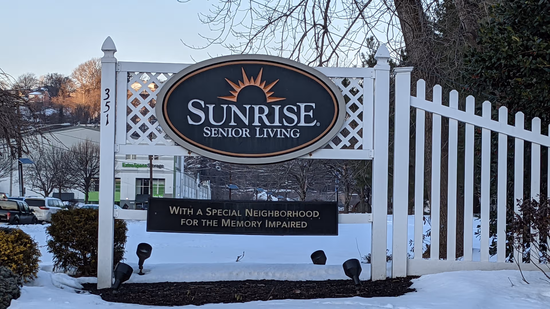 Sunrise Senior Living entrance sign with white lattice fence in snow.