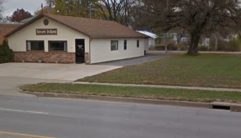 Single-story beige building with a sign for Tiffany In-Home Services by the street.