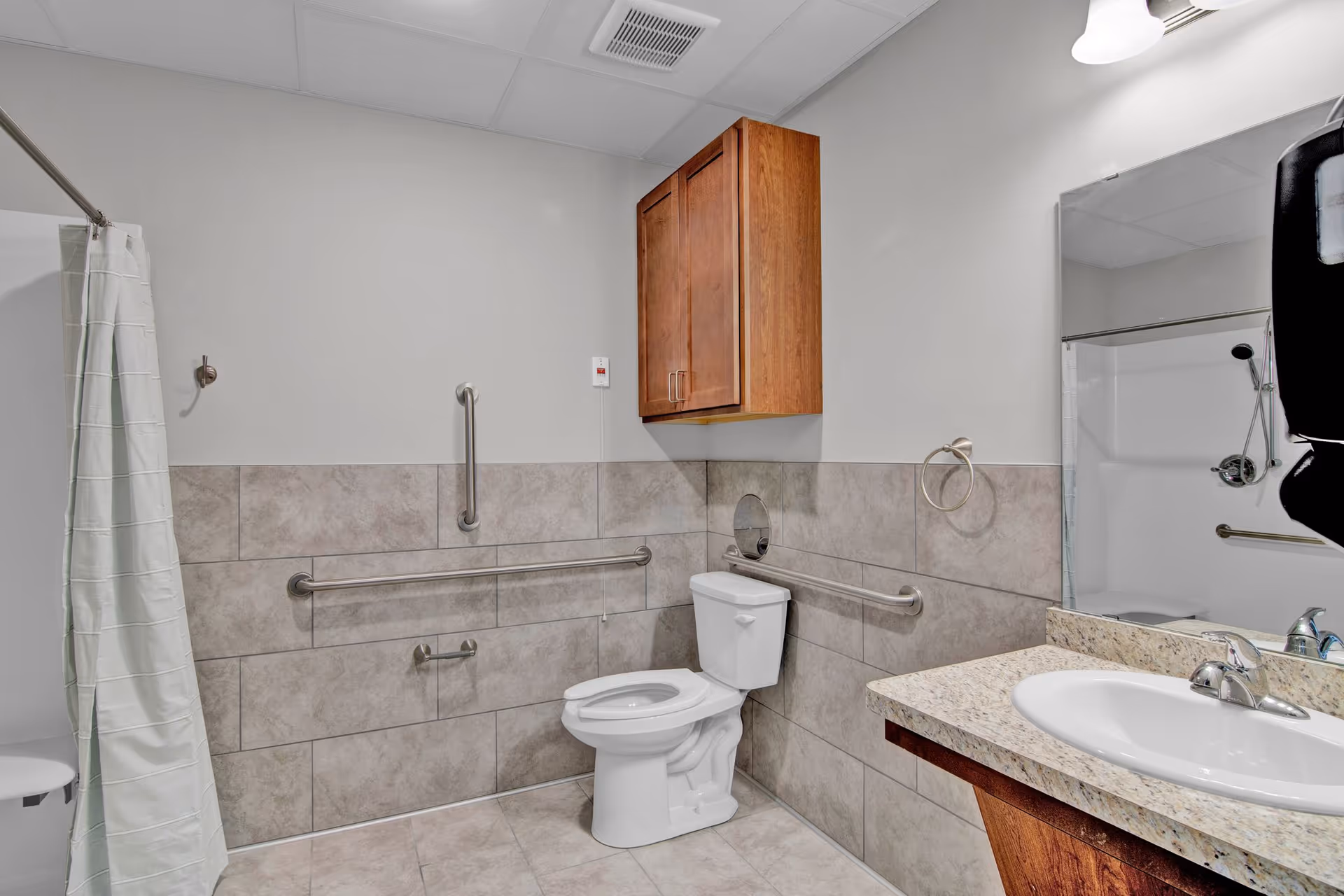 Accessible senior living bathroom with grab bars, toilet, sink, and shower.