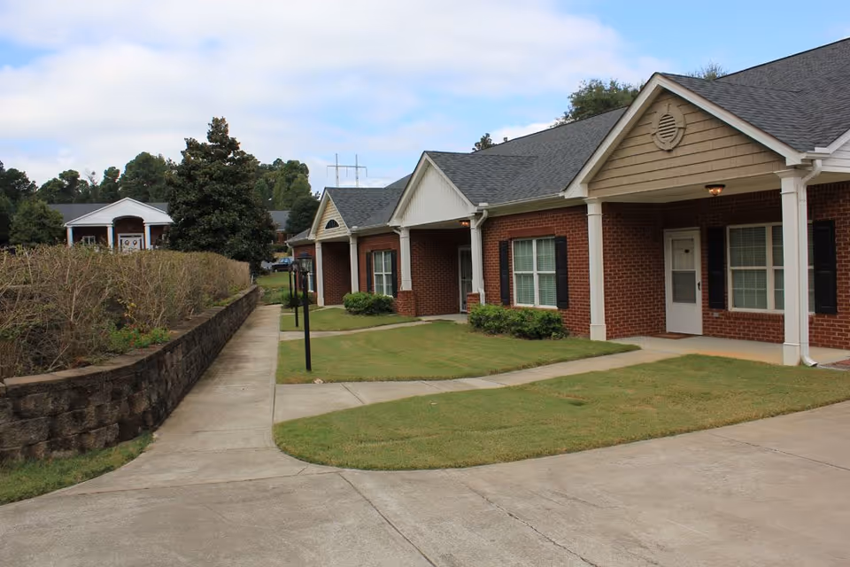 Single-story brick senior living building with covered porches, front lawns, and a walkway.