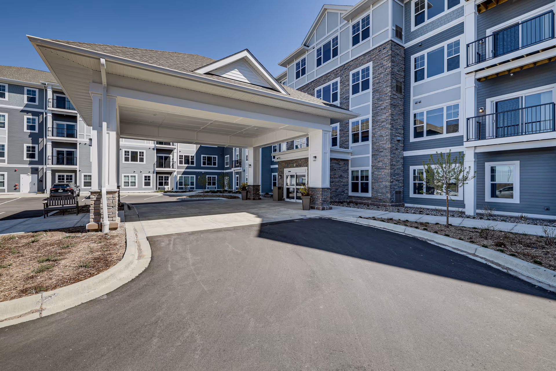 Covered porte-cochère and main entrance of a multi-story senior living building with balconies and stone accents.
