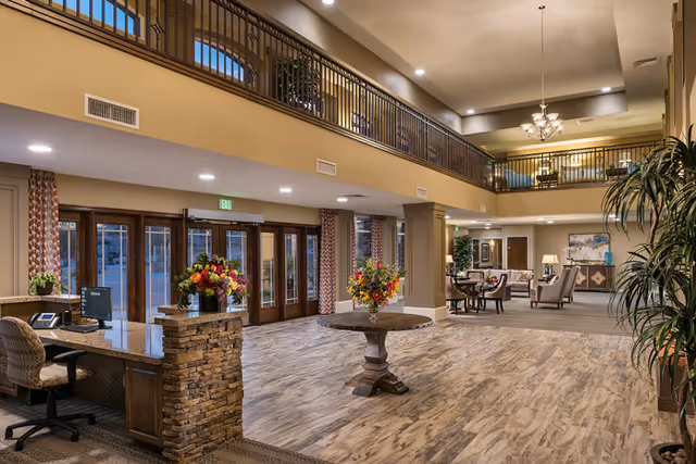 Spacious two-story lobby with a reception desk, central round table with floral arrangements, seating areas, and an upper balcony.