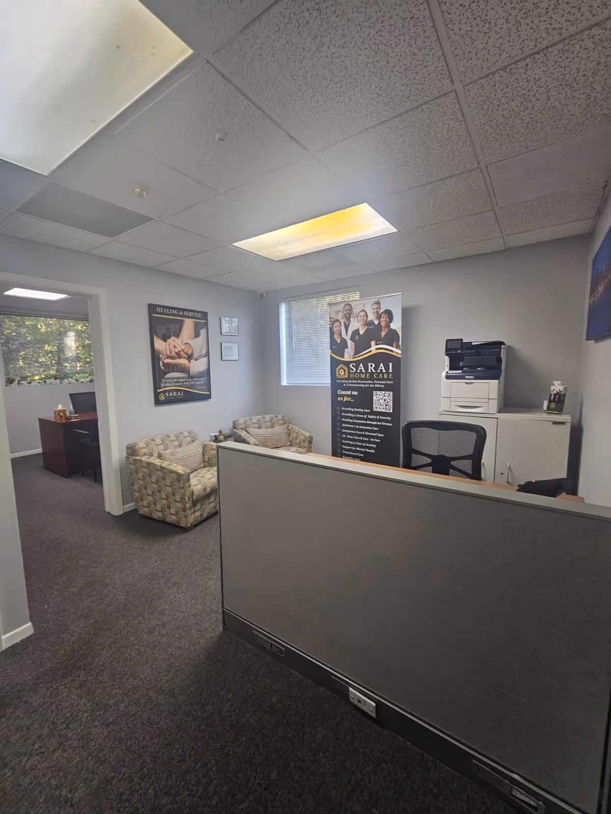 Reception area with a cubicle, two patterned chairs, posters, and a printer.