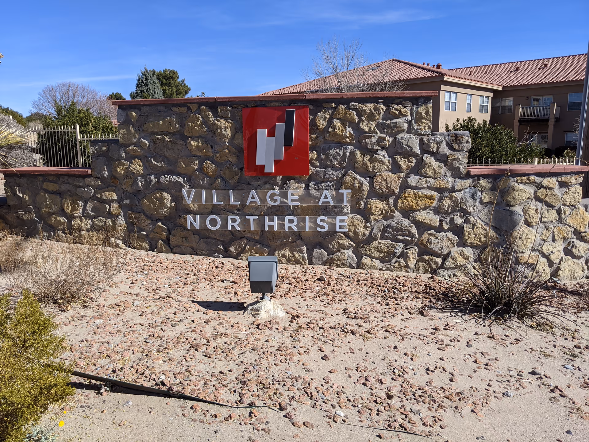 Stone entrance sign reading Village at Northrise with desert landscaping and a building behind.
