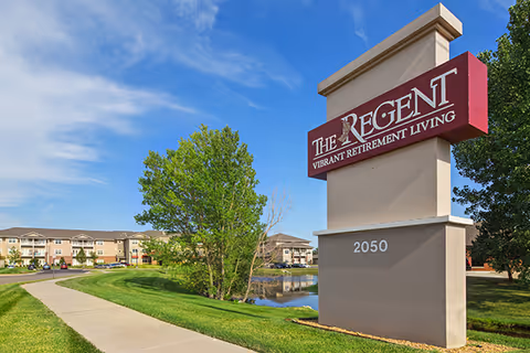 A large The Regent retirement living sign beside a sidewalk and green lawn.