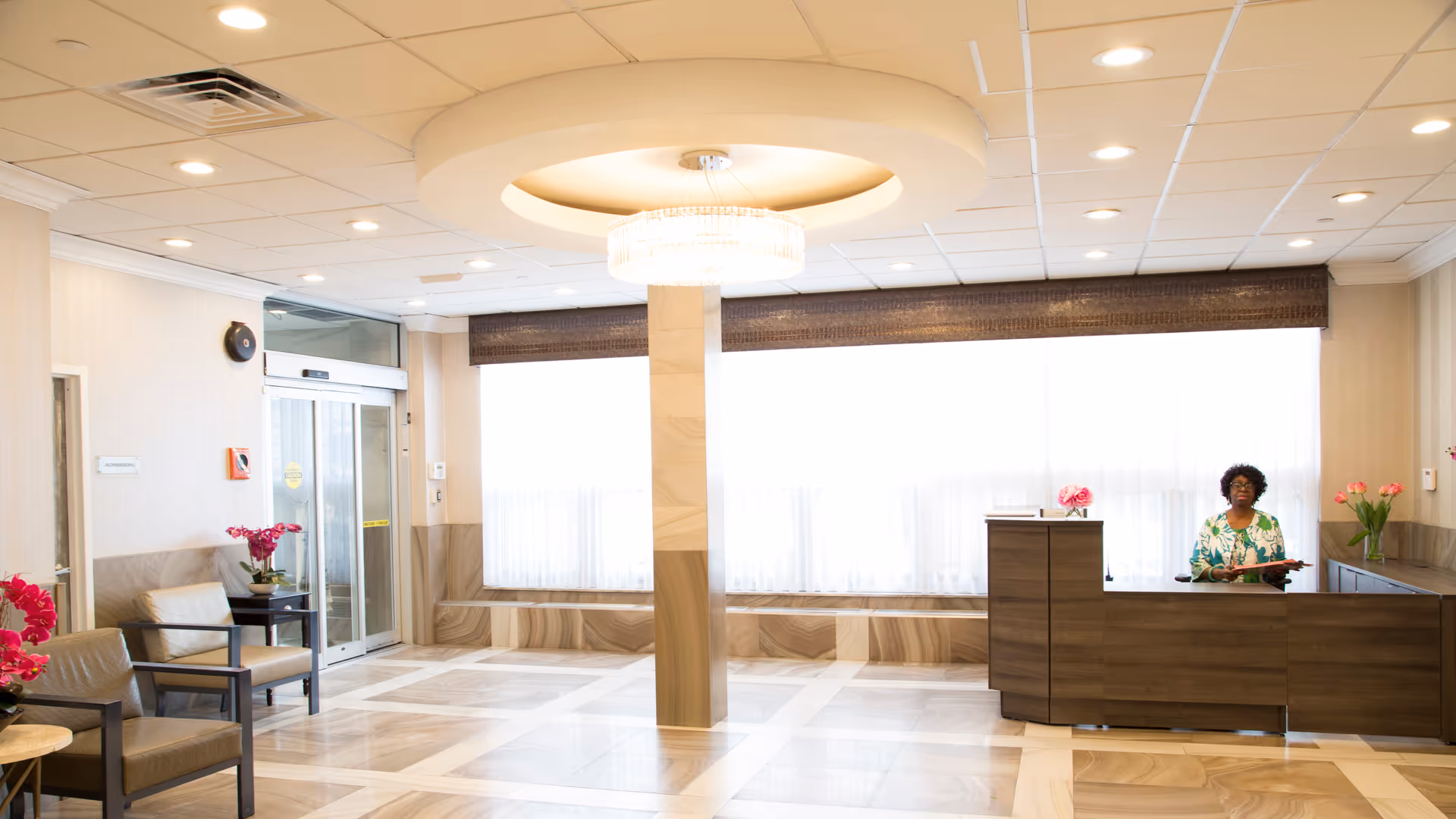Bright senior living facility lobby with reception desk, seating, and large windows.