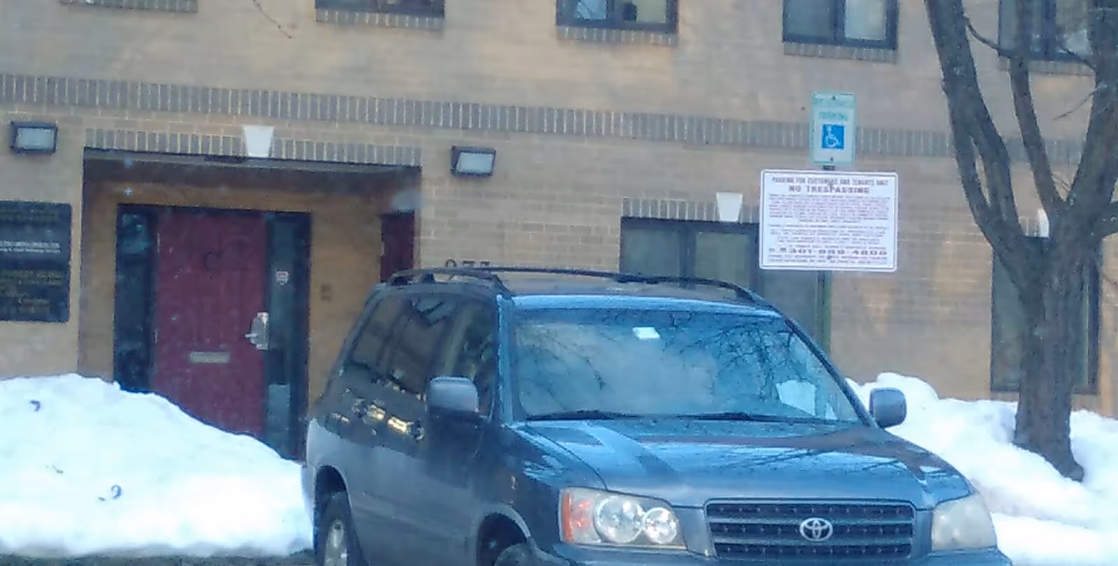 Exterior view of a brick senior care building with a blue SUV parked in snow.