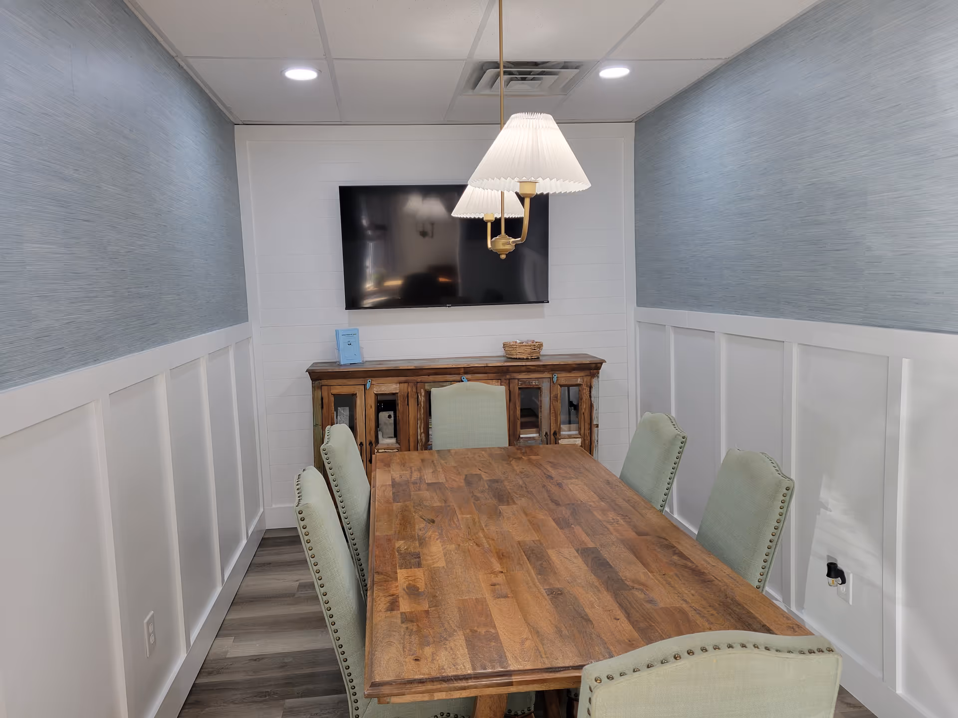 Dining room with a wooden table, green upholstered chairs, and a wall-mounted TV.
