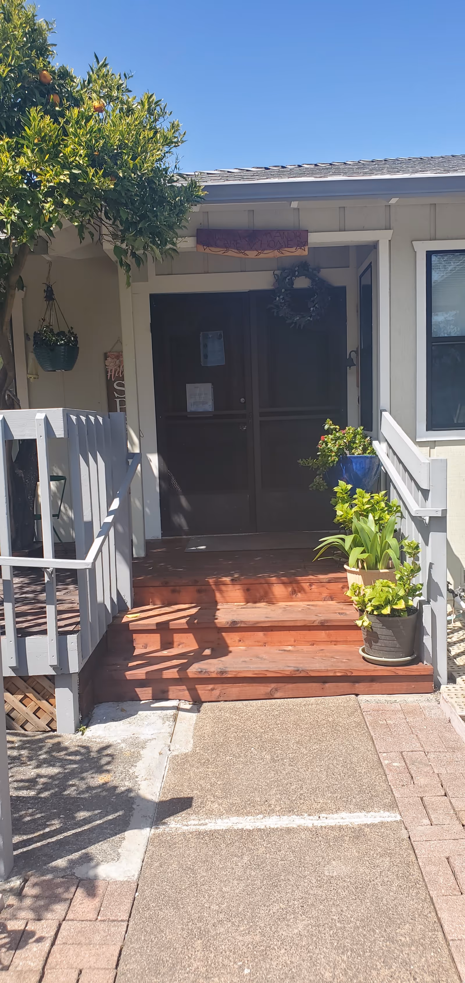 Exterior entrance of Adom Manor Care Home with steps, railing, and potted plants.