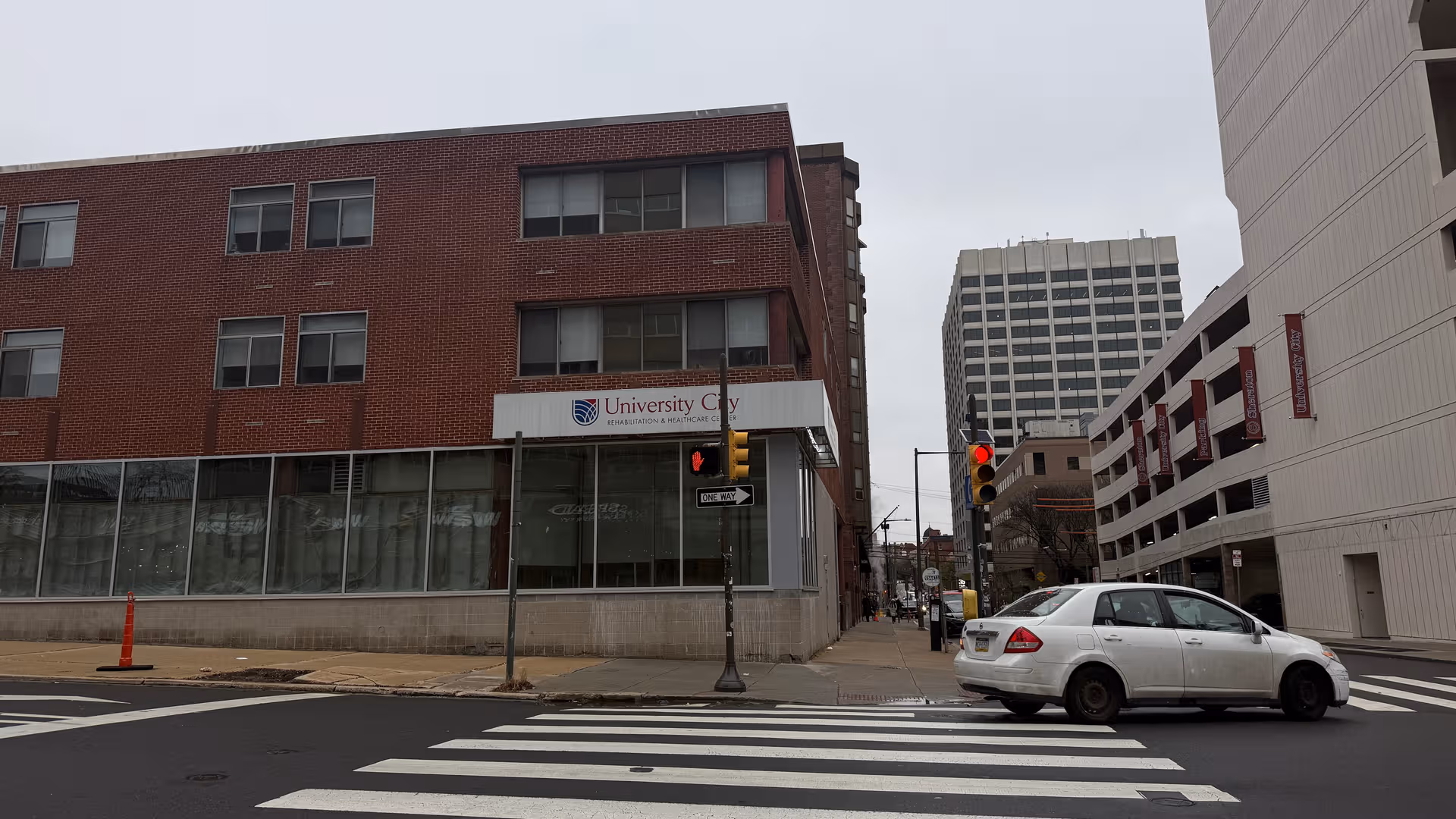 A brick building labeled University City Rehabilitation and Healthcare Center sits beside a crosswalk.