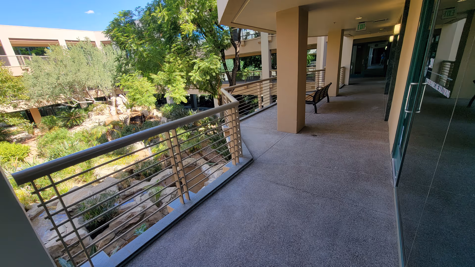 Outdoor corridor along the facility with railing, benches, and lush landscaping.