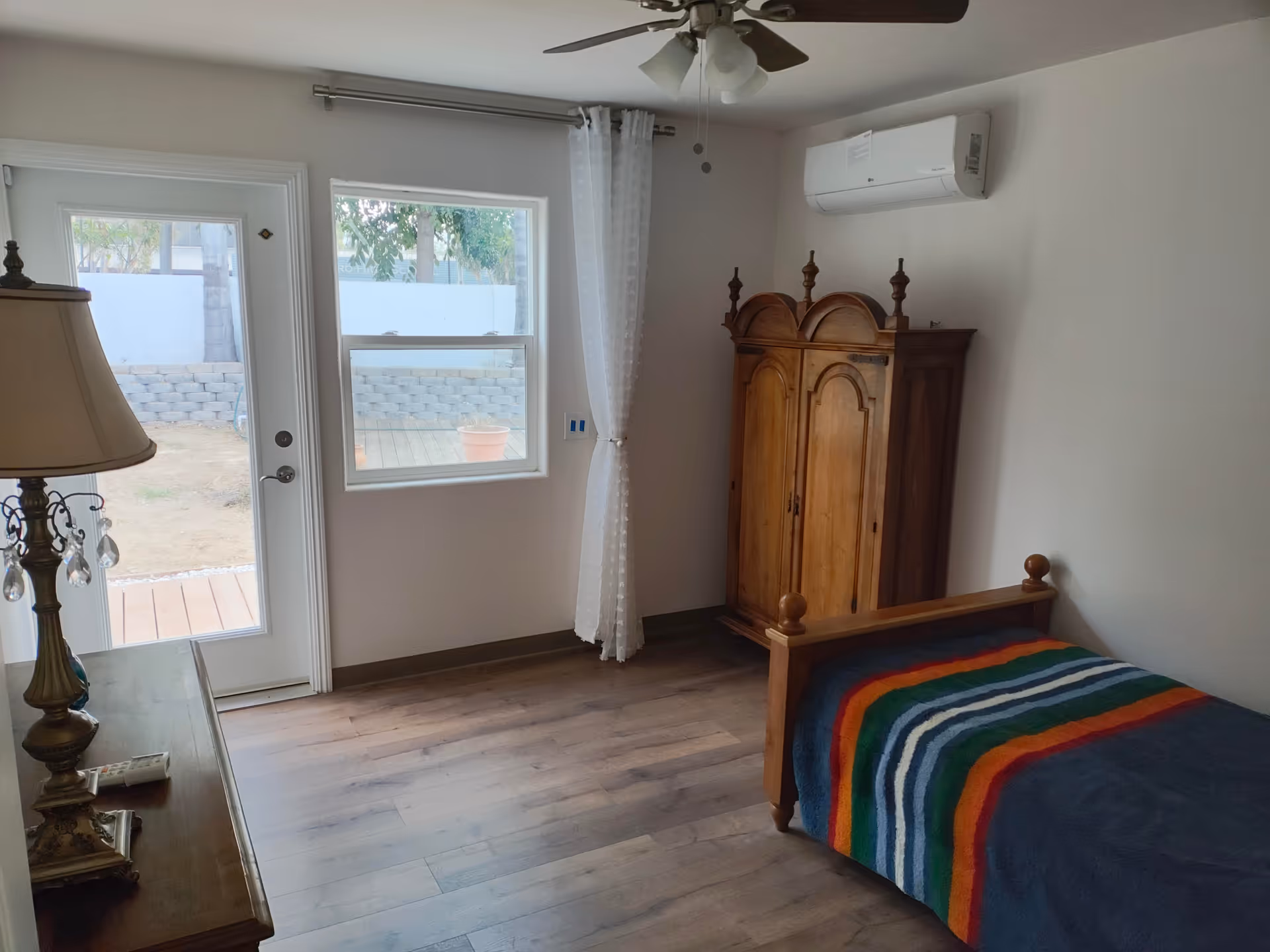 A tidy bedroom with a wooden armoire, single bed, dresser, ceiling fan, and window.