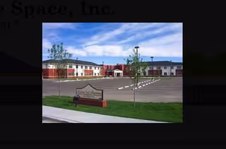Exterior view of Heritage Court Apartments, an affordable senior housing complex, with front entrance and parking.