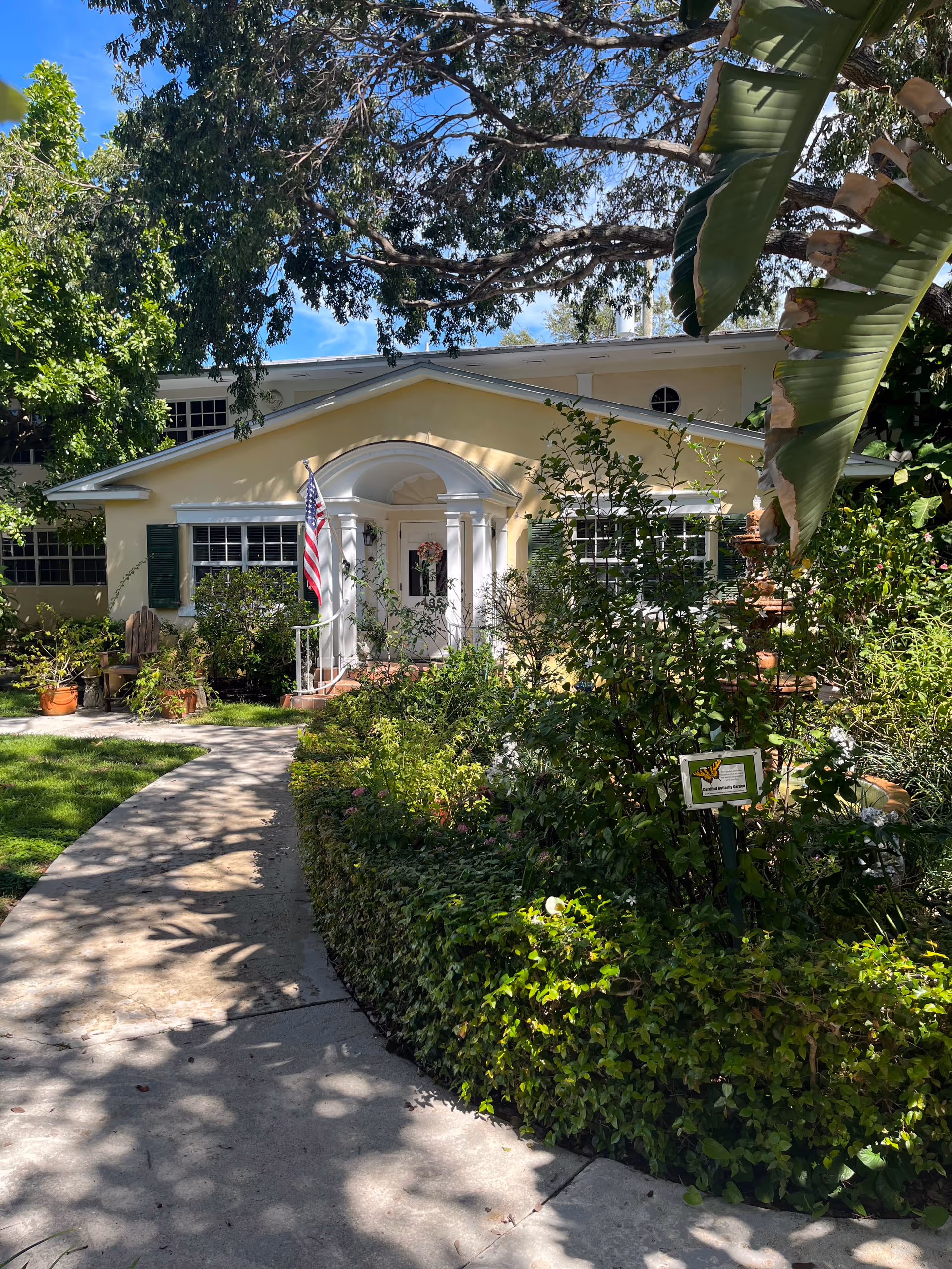 Yellow Bay Oaks senior living facility with a white front porch, flag, and lush garden path.