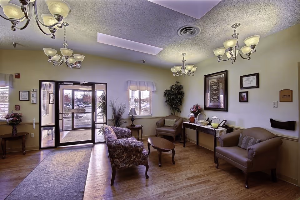 Well-lit senior living lobby with couches, glass entry doors, chandeliers, and a refreshments table.