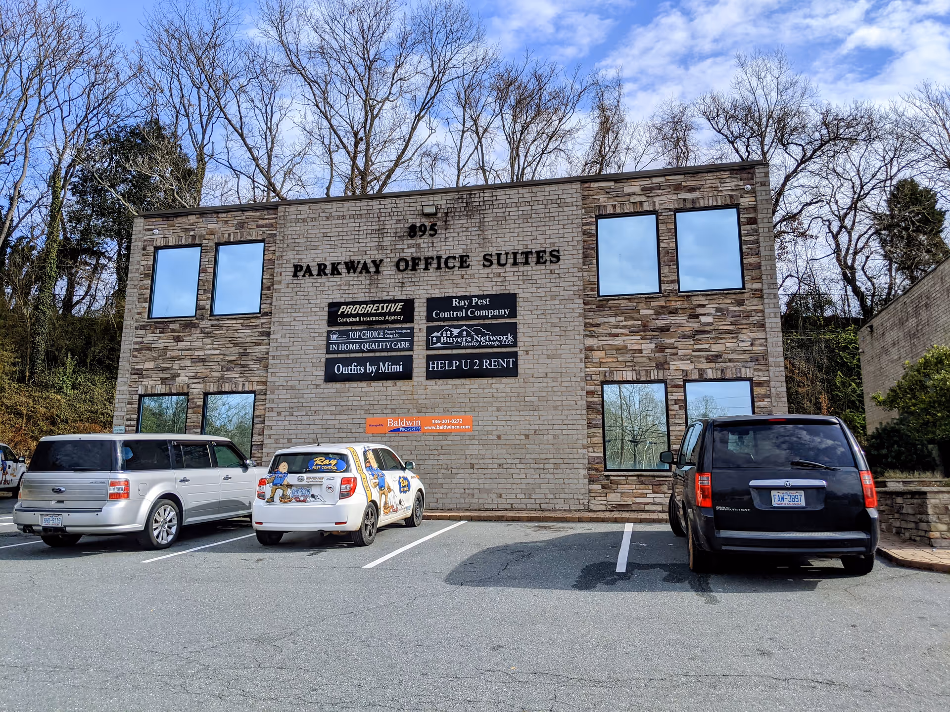 Brick building labeled Parkway Office Suites with signs and parked cars in foreground.