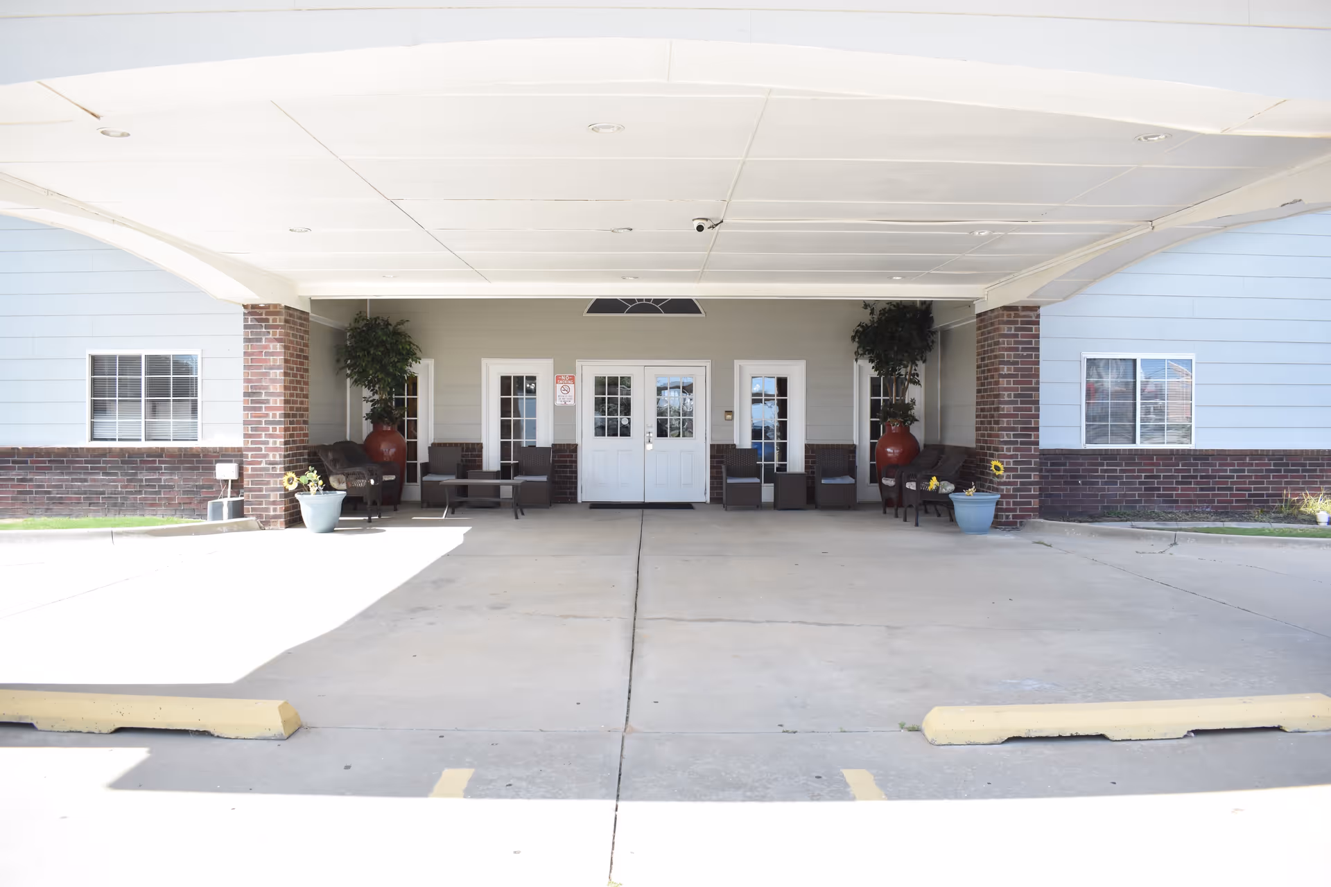 Covered front entrance of Featherstone Assisted Living Community of Moore with seating and double doors.