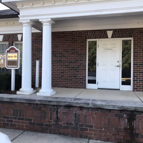 Brick building front with white columns and a white entry door.