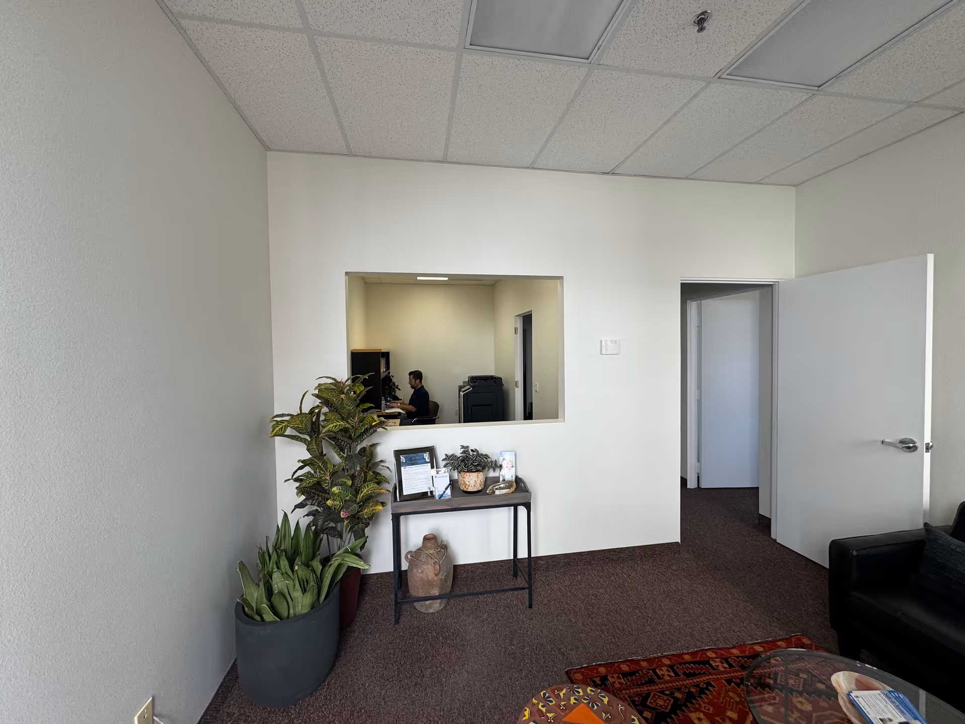 Reception area inside Canaan Home Care with a windowed desk, doorway, and potted plants.