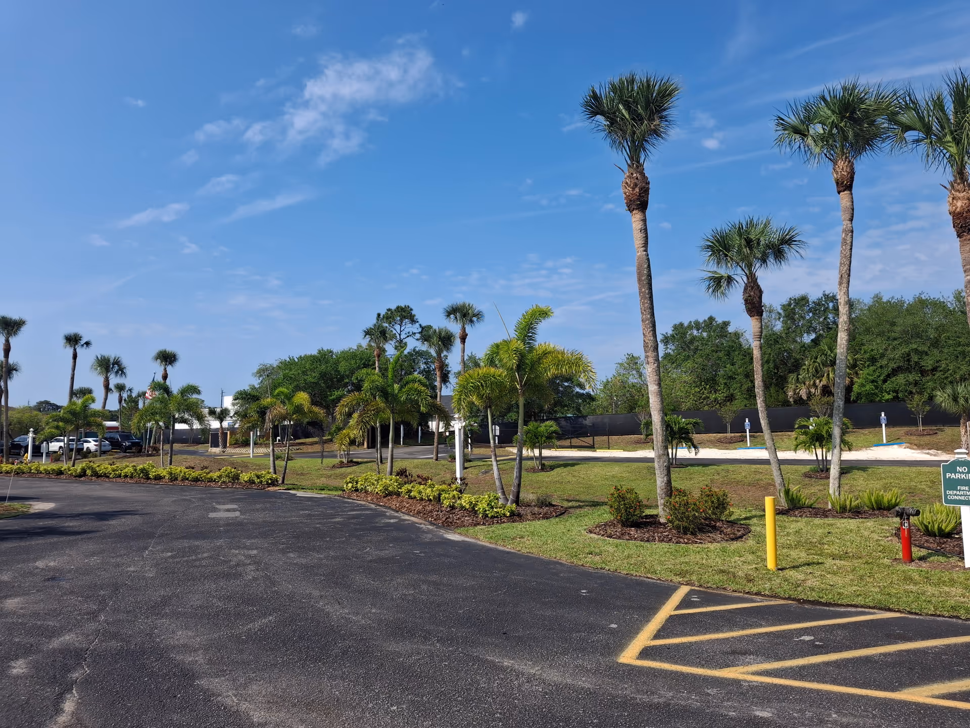 Sunny outdoor scene with palm trees, parking lot, and manicured lawns surrounding a senior living campus.