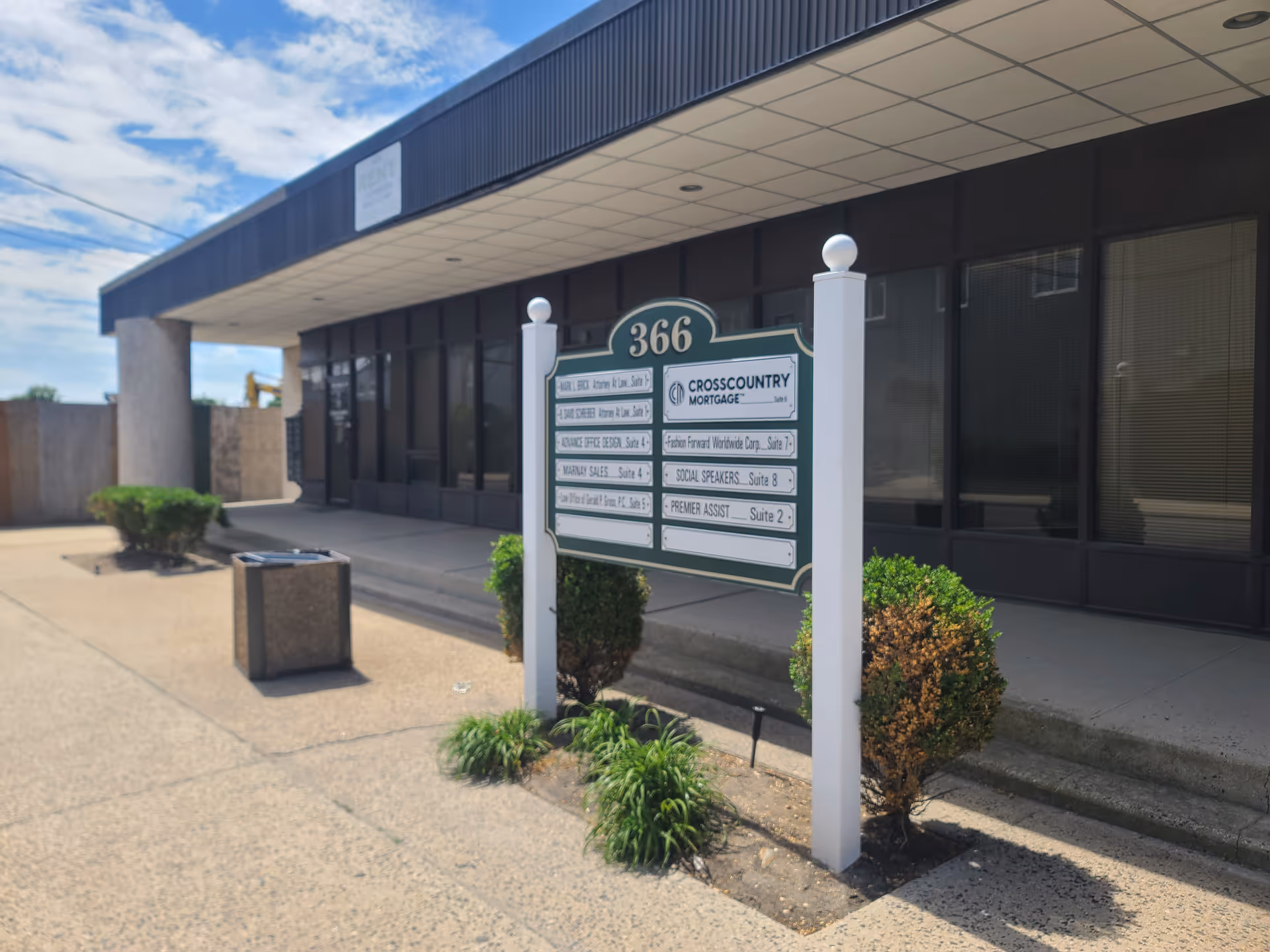 Front exterior of a commercial building with a sign post and shrubs.