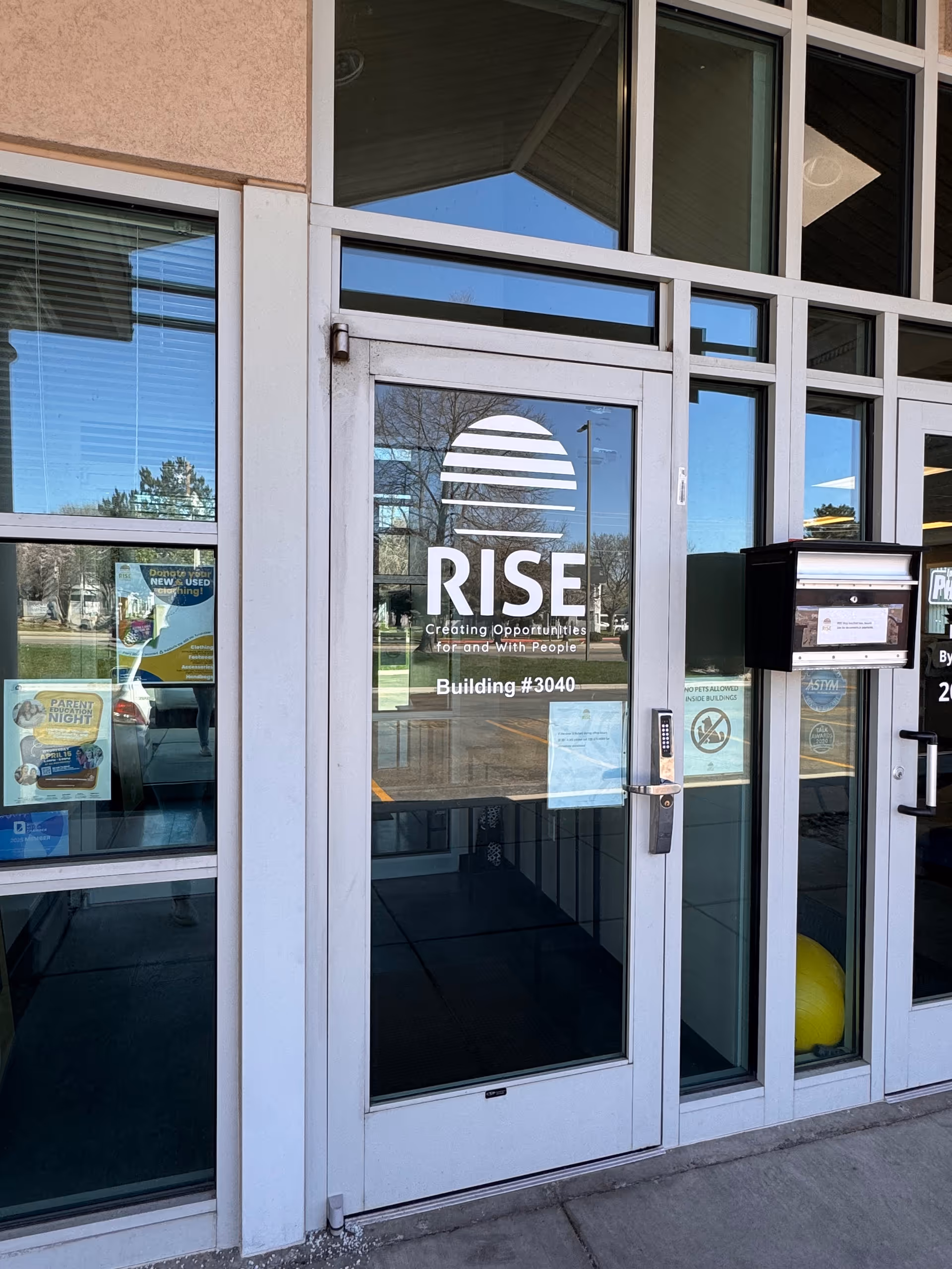 Glass entrance door displays RISE logo and building number, reflecting surrounding outdoor scene.