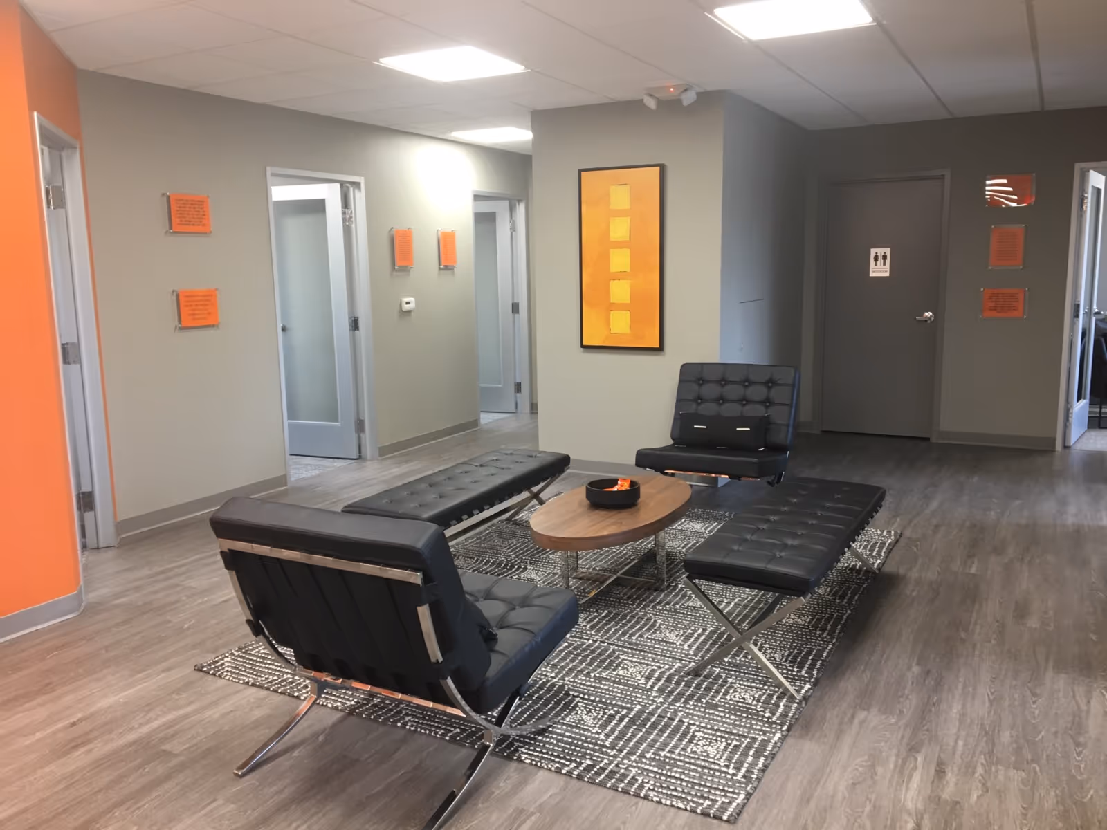 A modern lounge area with black tufted chairs, a round coffee table, and orange accent wall.