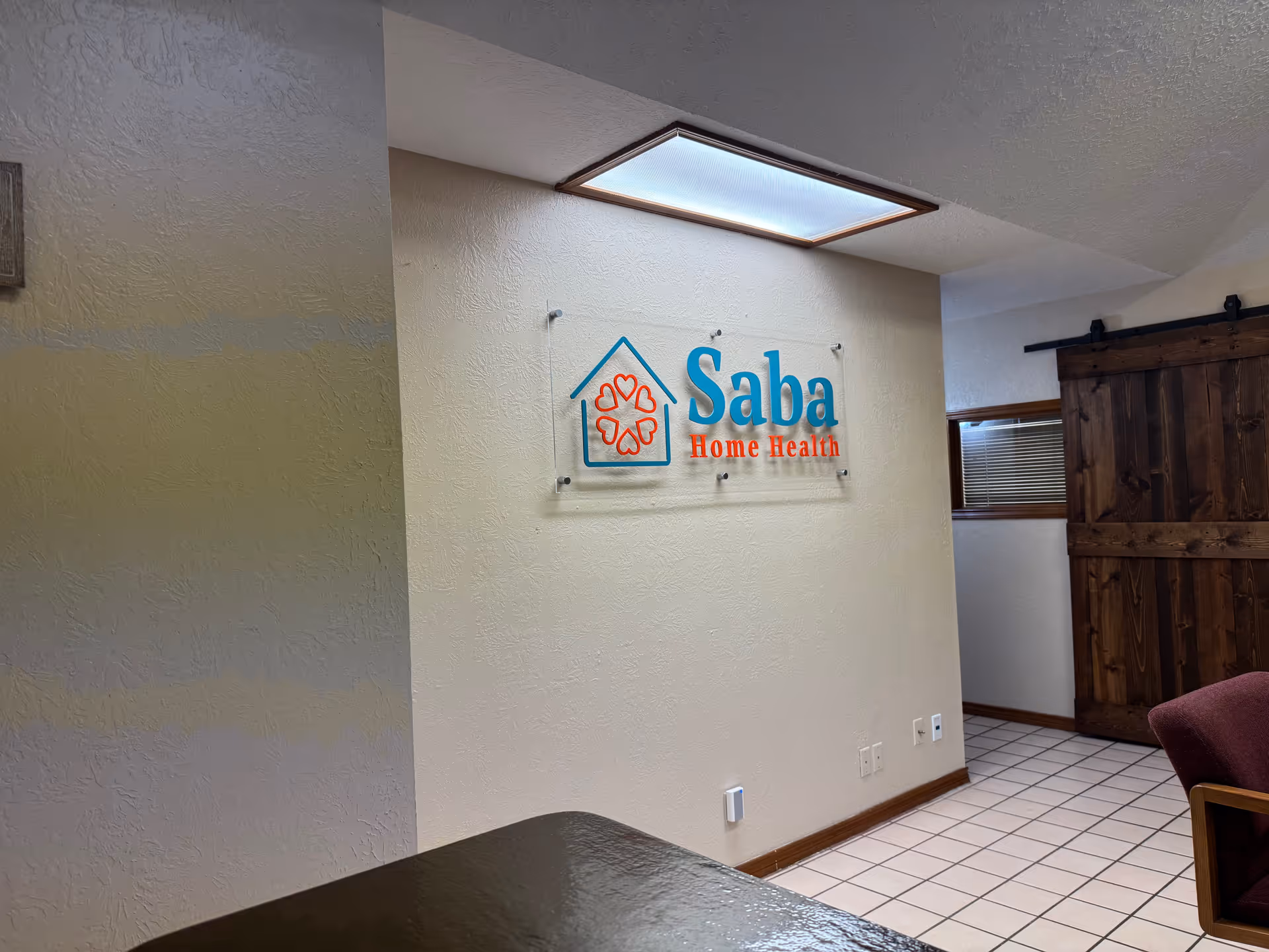 Indoor lobby area with a Saba Home Health sign on a beige wall.