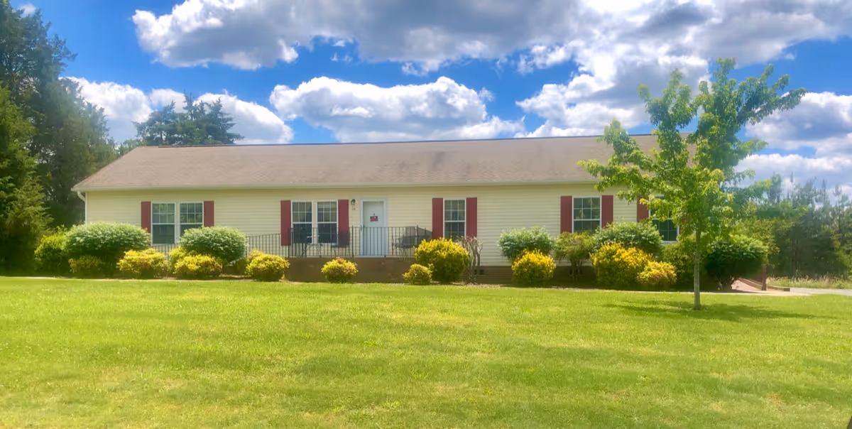 Single-story beige building with red shutters on a green lawn under blue sky.