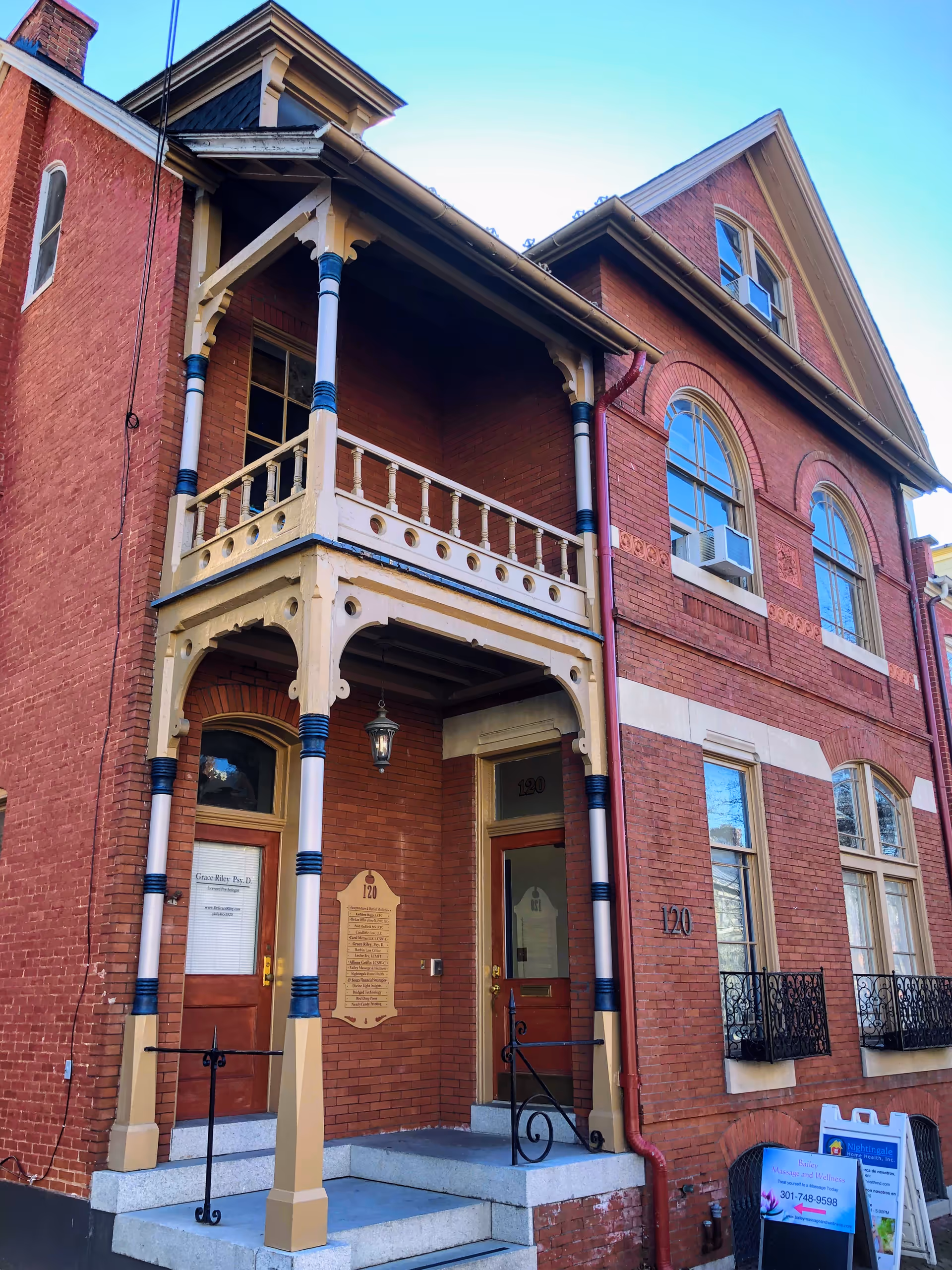 Historic brick building with a two-story porch, decorative columns, and stairs at the entrance.