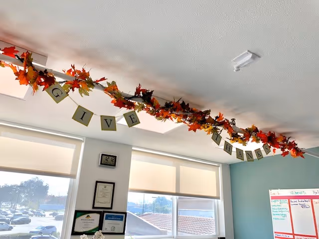 Autumn garland and 'GIVE THANKS' banner decorate a bright interior room with large windows.