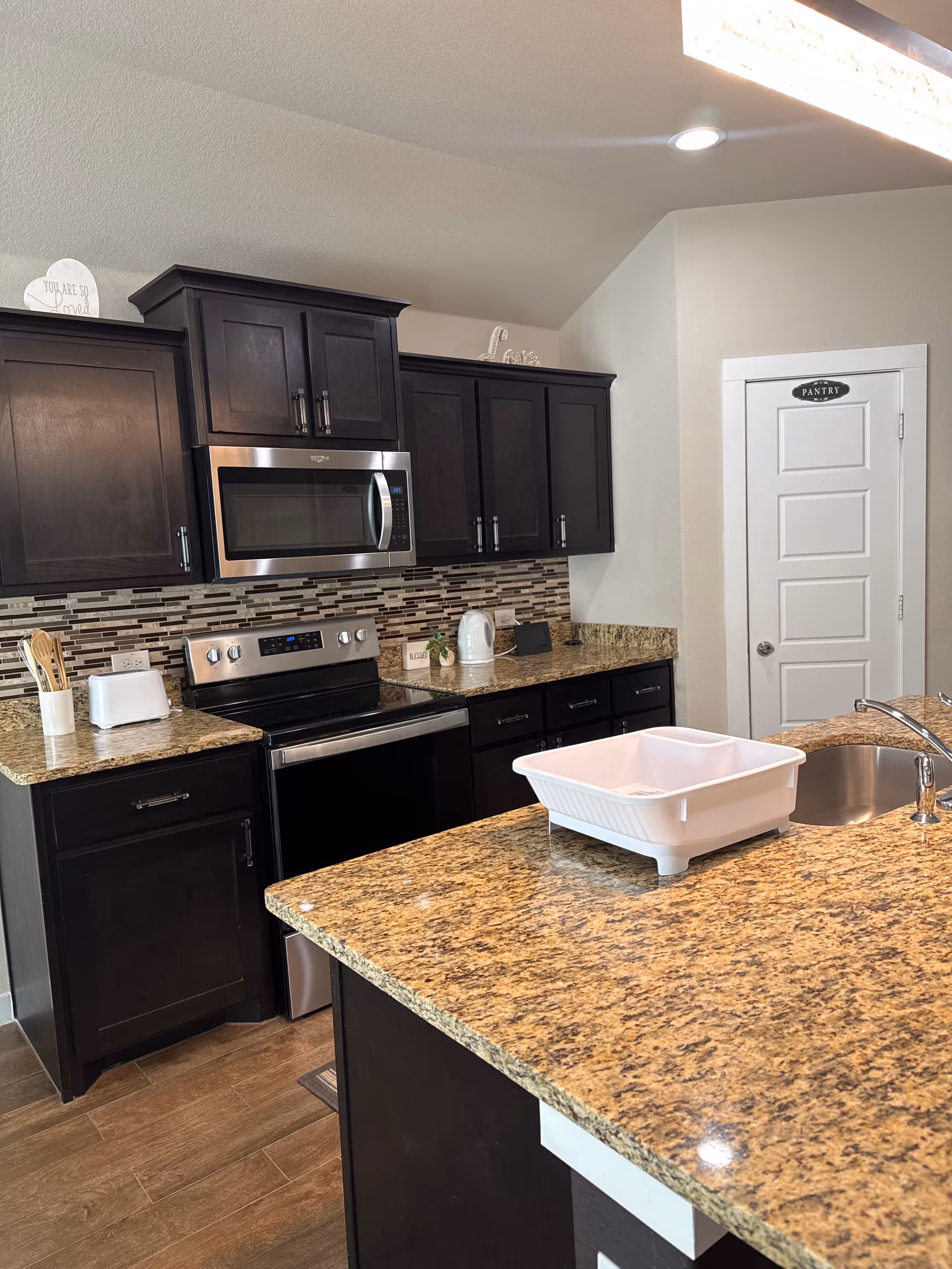 Modern kitchen in a senior living facility with dark cabinets, granite counters, and stainless appliances.